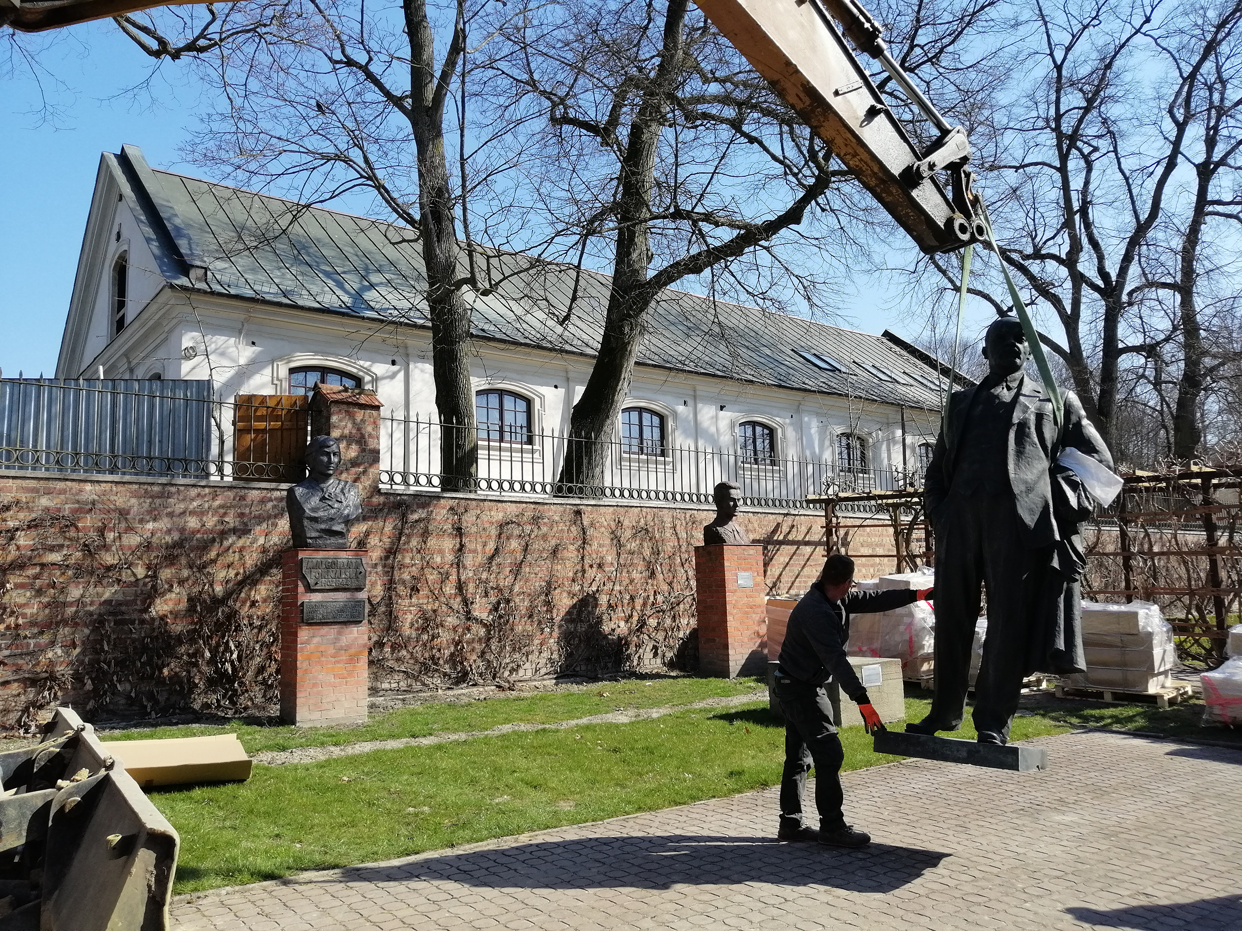 Pomnik Włodzimierza Lenina, postać całościowa. Rzeźba z brązu o wymiarach 260 x 120 x 75 cm uniesiona nad ziemię za pomocą pasów holowniczych. Po lewej stronie mężczyzna podtrzymujący rzeźbę. Fotografia. Pomnik Włodzimierza Lenina, postać całościowa. Rzeźba z brązu o wymiarach 260 x 120 x 75 cm uniesiona nad ziemię za pomocą pasów holowniczych. Po lewej stronie mężczyzna podtrzymujący rzeźbę.