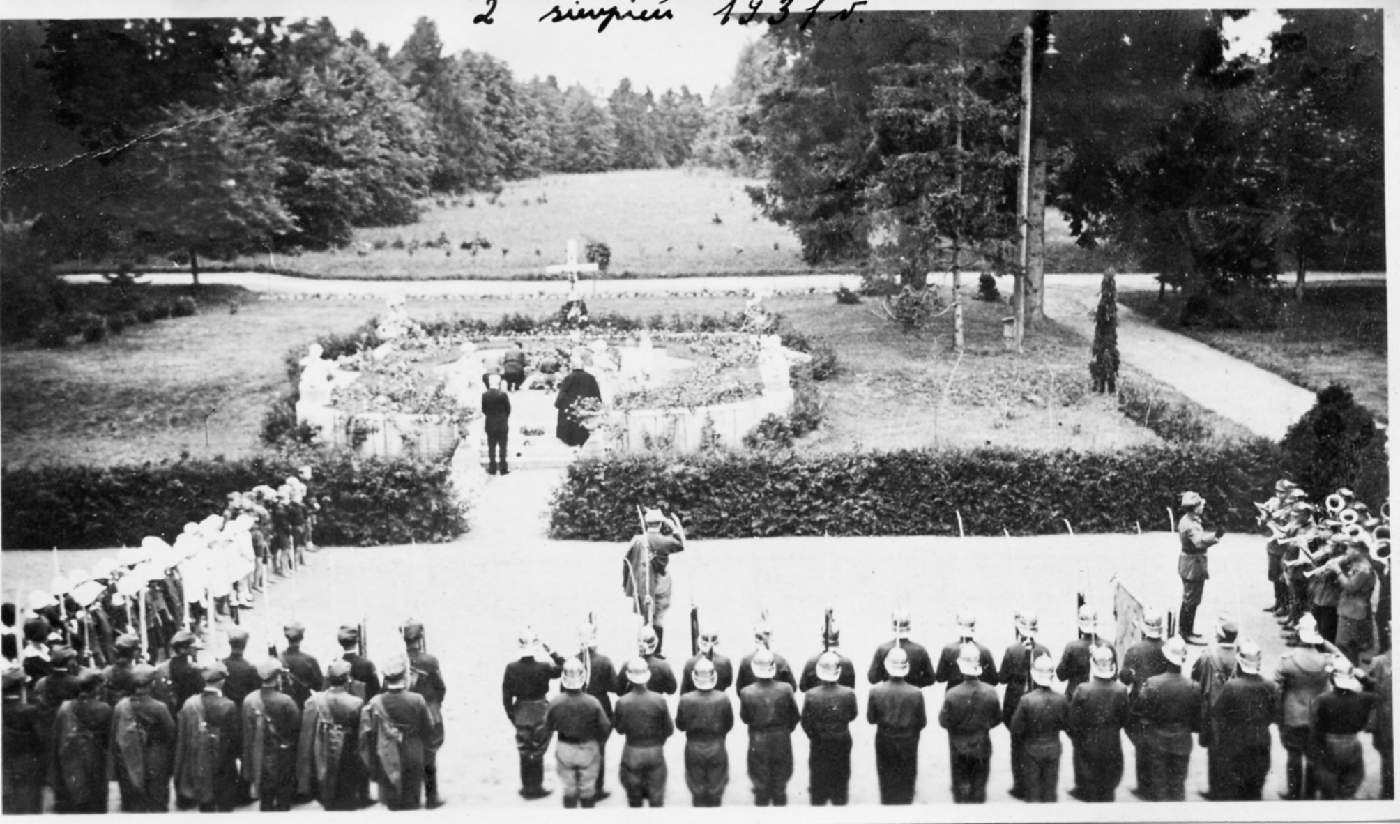 2. Uroczystości przy grobie Marii Zamoyskiej, 2 sierpnia 1931 r.; ze zbiorów Jadwigi „Inki” Zamoyskiej Zdjęcie archiwalne, czarno-białe. Przed grobem ziemnym, obsadzonym krzewami i udekorowanym różnorodnymi kwiatami, ustawione w dwuszeregu oddziały Towarzystwa Gimnastycznego „Sokół”, w tym straż pożarna, widoczne od tyłu. Po prawej widoczna orkiestra dęta, po prawej grupa dzieci. Przed grobem grupa mężczyzn składająca wieniec oraz dwie postacie stojące. Na grobie krzyż.