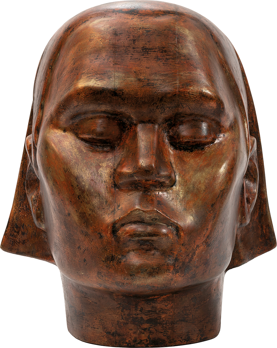 Janusz Wilden, Głowa Janusz Wilden
1906 Warszawa – 1991 Warszawa
Głowa
powstała w 1957 roku
Drewno polichromowane
30 x 27 x 32 cm
Muzeum Zamoyskich w Kozłówce
MPK/SW/690
Przed nami imponująca rzeźba dużej, idealizowanej głowy wykonanej z ciemnego, polichromowanego drewna, którego głęboka barwa nadaje dziełu szlachetność i powagę. Twarz, choć uproszczona i pozbawiona naturalistycznych detali, zachwyca symetrią i monumentalnością formy. Szerokie policzki, masywny, szeroki nos oraz pełne, lekko zaciśnięte usta tworzą wyraz siły i godności.
Oczy – zamknięte, z wyraźnie zarysowanymi powiekami – sprawiają, że twarz zdaje się być pogrążona w medytacyjnym skupieniu. Gładkie czoło oraz wysokie kości policzkowe podkreślają niemal architektoniczną strukturę, nadając rzeźbie charakter symboliczny i ponadczasowy.
Włosy zredukowane do prostych, gładkich płaszczyzn opadają po bokach głowy, przypominając hełm lub ciężką kotarę, co wzmacnia wrażenie spokoju i powagi. Ta minimalistyczna forma jest wyrazem skupienia i wewnętrznej siły, jakby głowa stała się ucieleśnieniem duchowej obecności.
Całość zachwyca klarownością, równowagą i intensywną prostotą, które przenoszą widza w przestrzeń medytacji i refleksji nad istotą bytu.